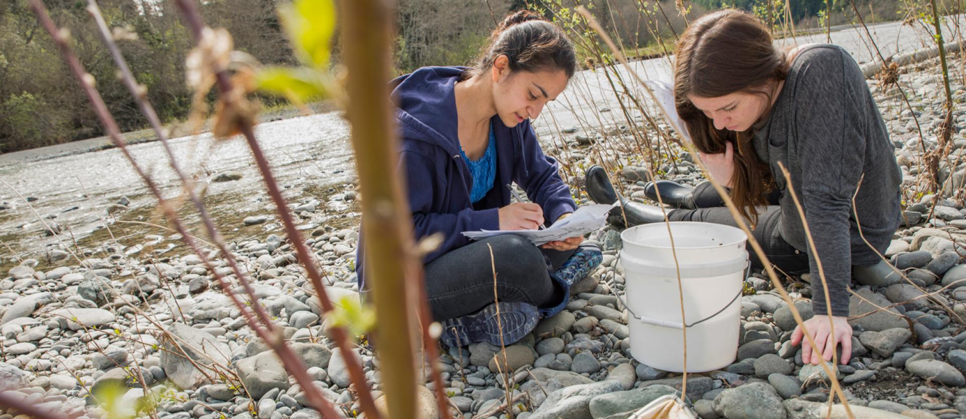 two students sitting by the river taking samples