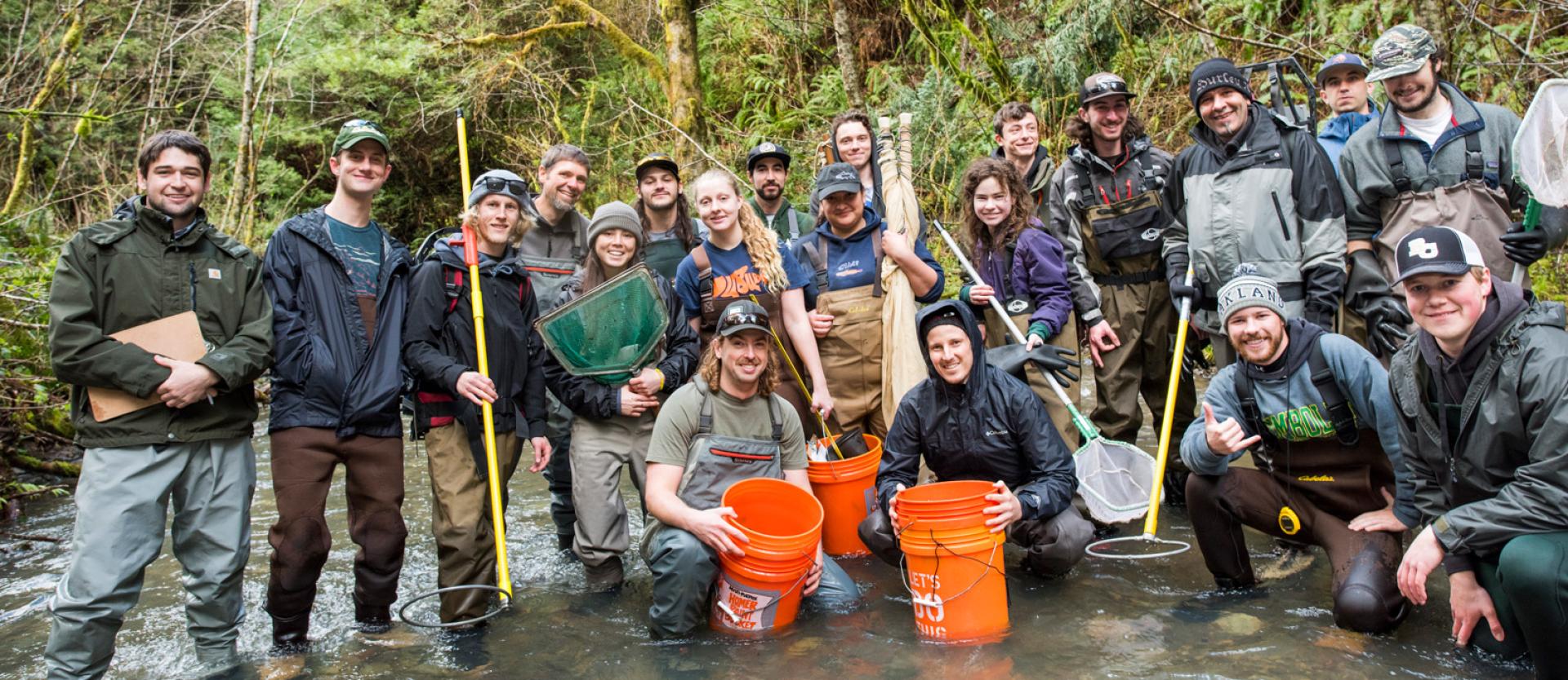 large group of students with equipment standing in a river