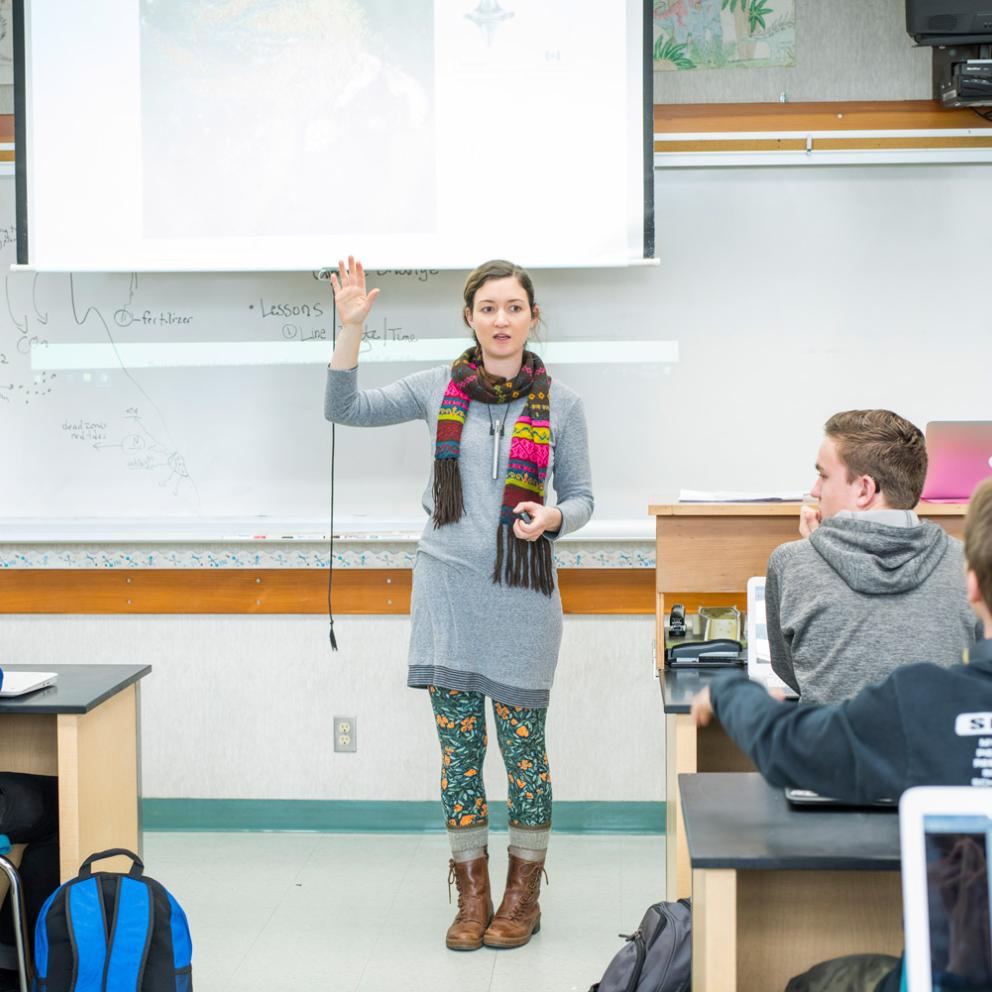 Student standing in front of a class raising her hand