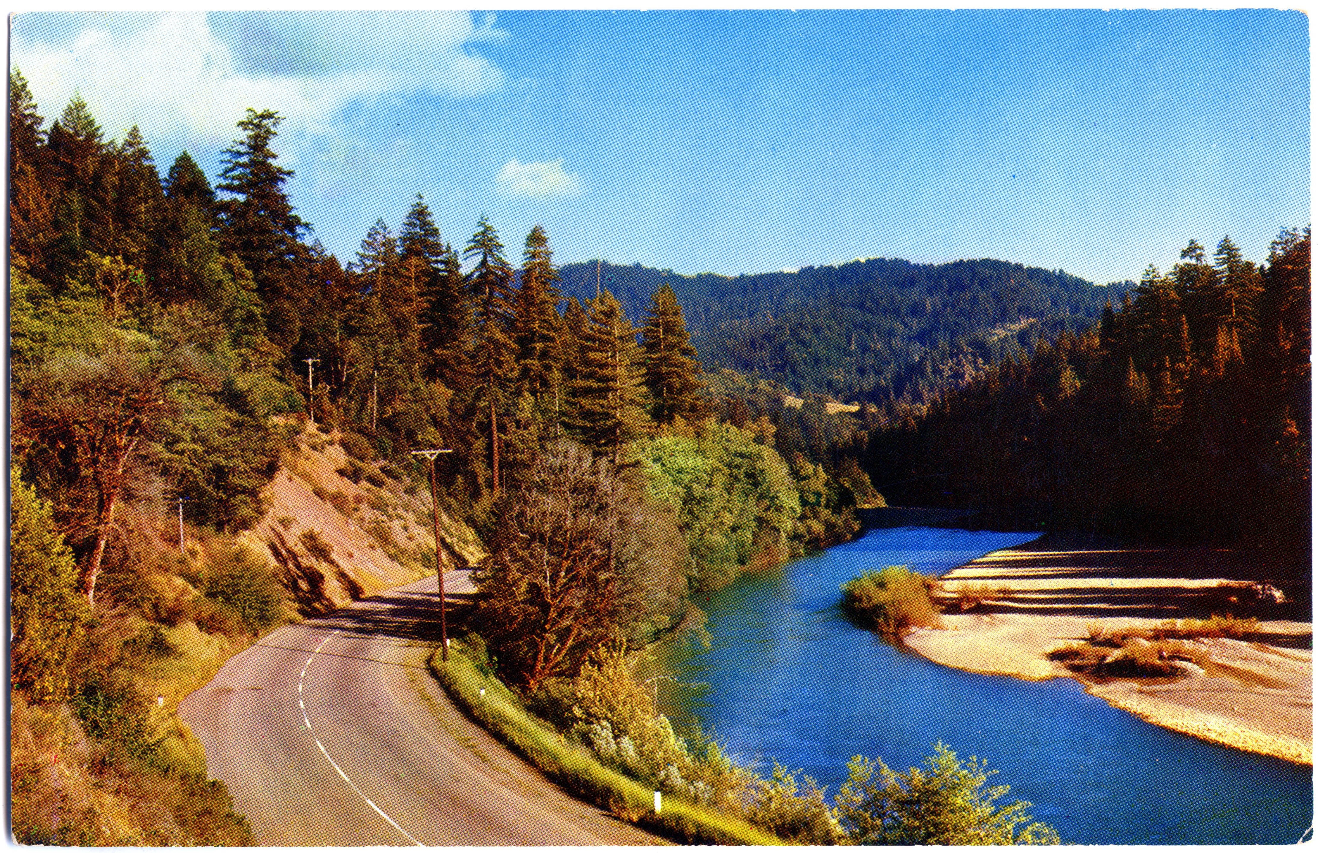 Color photo of highway winding around river bend with lush forest all around