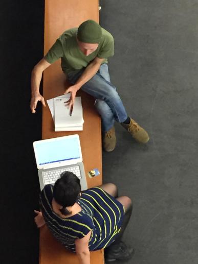 Two people sitting on a bench with a computer and papers