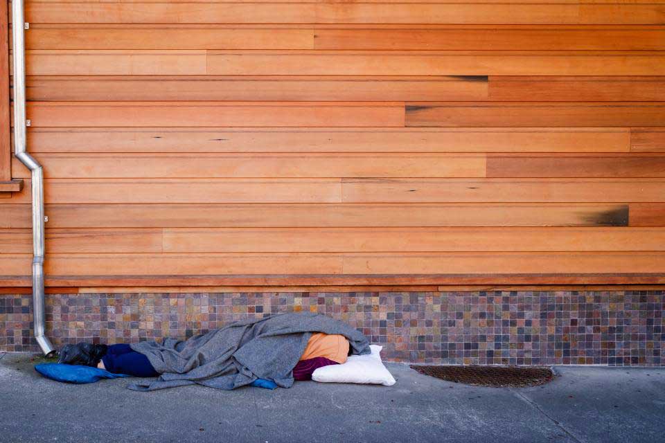 Person sleeping on sidewalk in front of wall