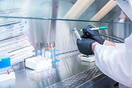 Two hands with black gloves marking a test tube with other test tubes on the table next to the hands