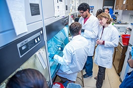Three people in a lab with white lab coats working with equipment