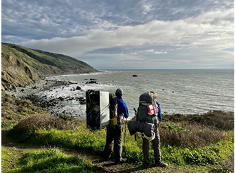 Two backpackers on a trail looking out at the oceam