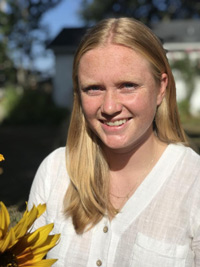 Claire outside with a white shirt and yellow flower, smiling for the camera