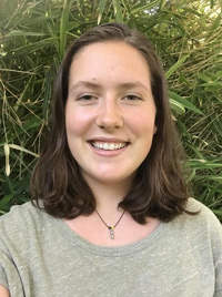 Malia portrait, wearing a light green shirt, grass background, and shoulder length brown hair