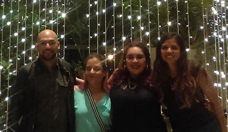 four people with arms over shoulders smiling for the camera in fron of a star lit wall