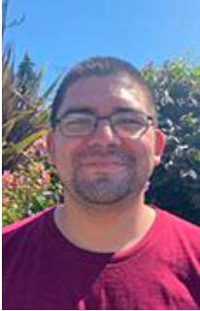 portrait of Ernesto standing outside in front of some bushes with a blue sky