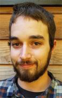 Joshua standing in front of a wood slat building, closeup portrait