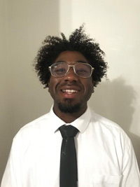 Jason with a white shirt and a black tie standing in front of a white wall, smiling for the camera