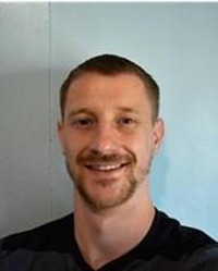 Austin's portrait, wearing a black shirt, goatee, and a white wall behind him