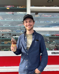 Roland standing in front of a window full of model cars holding an ice cream