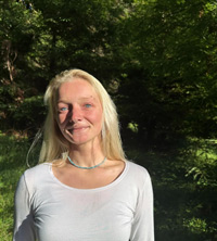 Lucille smiling for the camera wearing a white shirt standing in front of some trees and grass