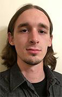 Tyler portrait up close wearing a dark green shirt and shoulder length hair pushed behind ears