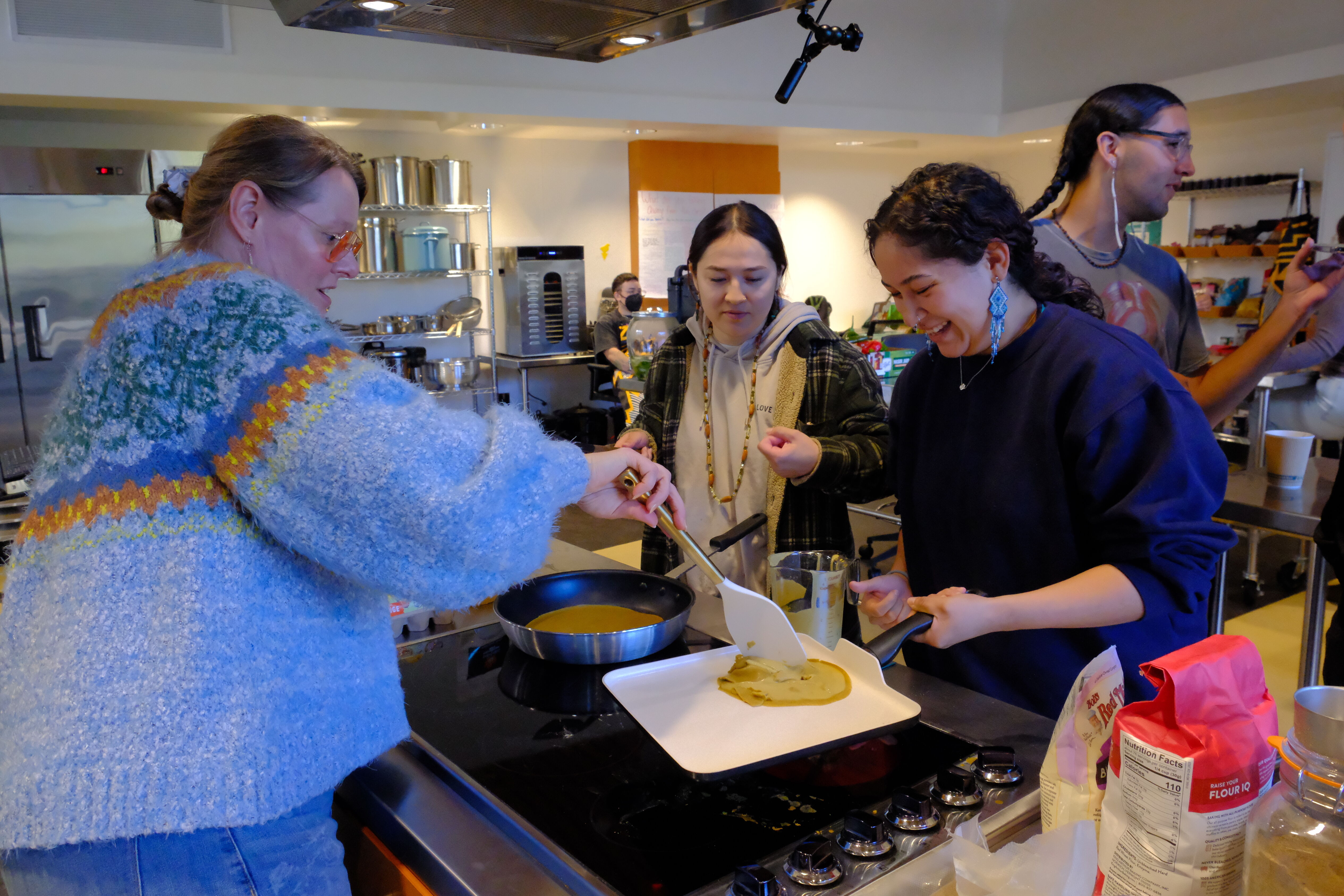On the left is Chef Sara Calvosa cooking Acorn Crepes with some students during a workshop.