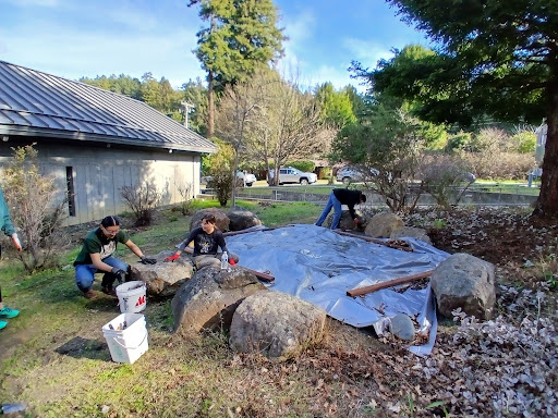 3 FSL Volunteers and Staff cleaning up around the Salmon Cooking Pit.