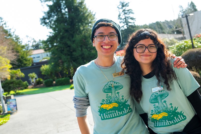 Two students in glasses and matching Humboldt shirts smiling and hugging.