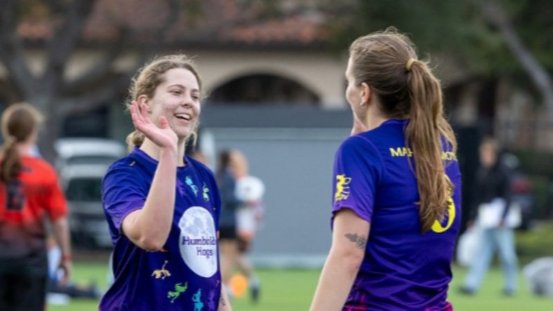 Two women's ultimate frisbee players high five-ing on the field.