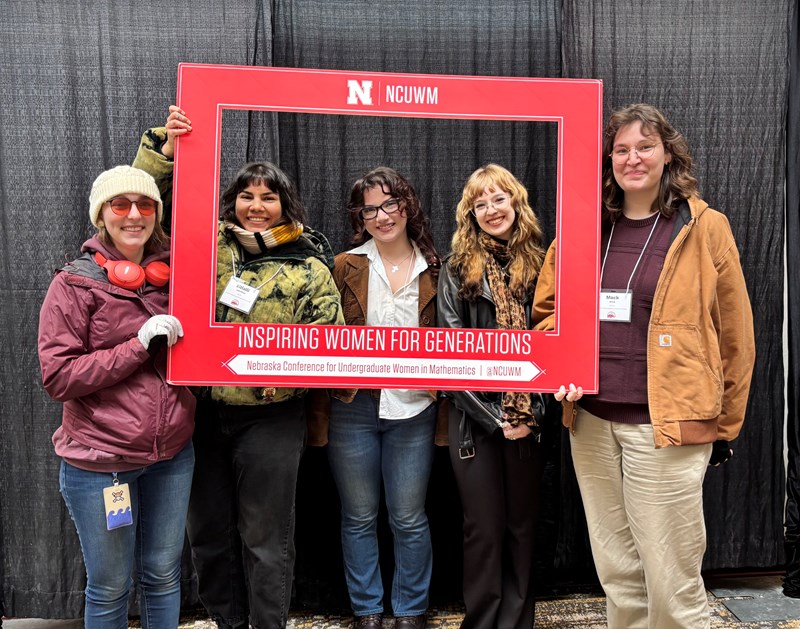 Five women math majors standing with a giant red frame at a math conference.