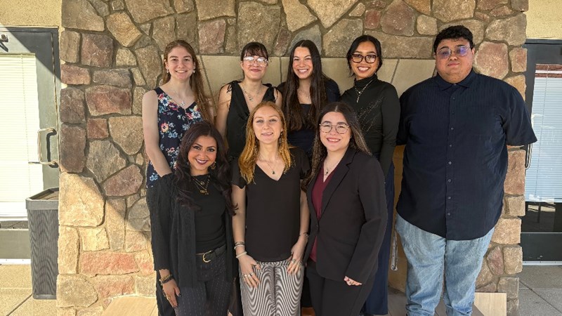 Eight Psychology members in a group smiling in front of a rock wall.