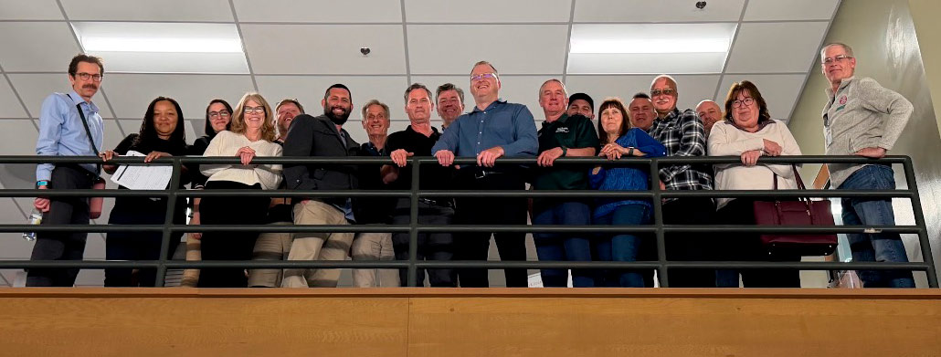 A large group of people standing in front of a balcony rail smiling for the camera