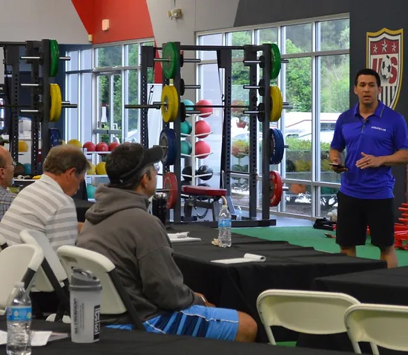 someone wearing a bright blue shirt standing in a weight room giving a talk