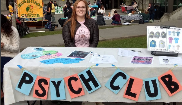 table with the words psych club and a student sitting behind it.