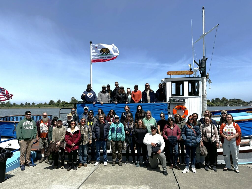 Image depicts numerous members of the Sea Level Rise Institute standing in front of a research vessel.