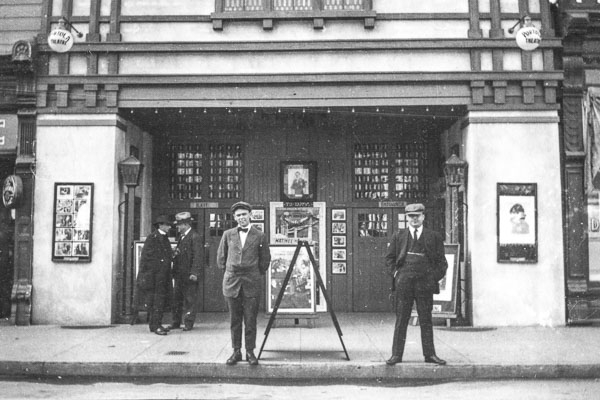black and white photo of a man in a suit standing in front of a theater