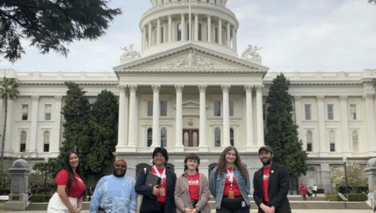 Six students wearing CSSA t-shirts stand before the California capitol building