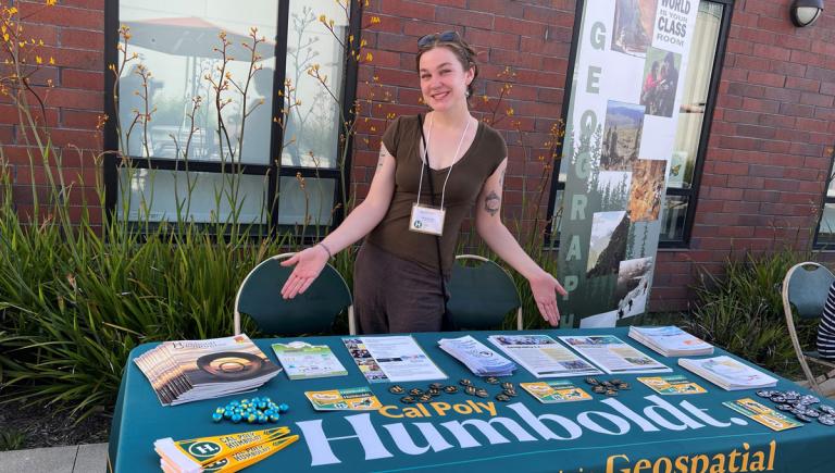 Student standing in front of a table with Cal Poly Humboldt goodies on it
