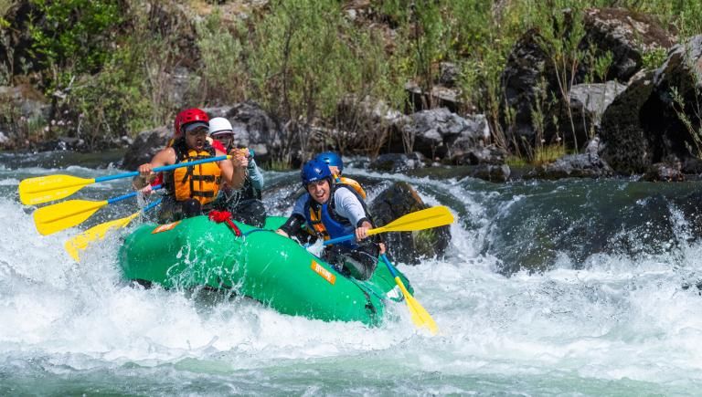 A small green raft going through a rapid. 