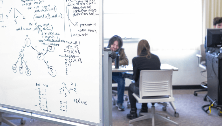 Two People at desk with whiteboard in foreground
