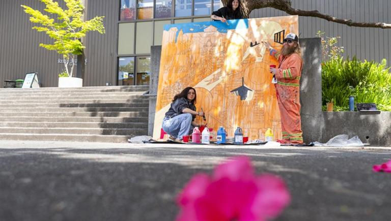 Two students, Alexia Friedman (top) and Mariah Kirkpatrick (bottom), and Art Education Professor James Woglom (right) paint a mural designed by Pelican Bay incarcerated artists.