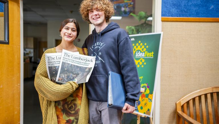 Two students holding printed issues of the Lumberjack newspaper