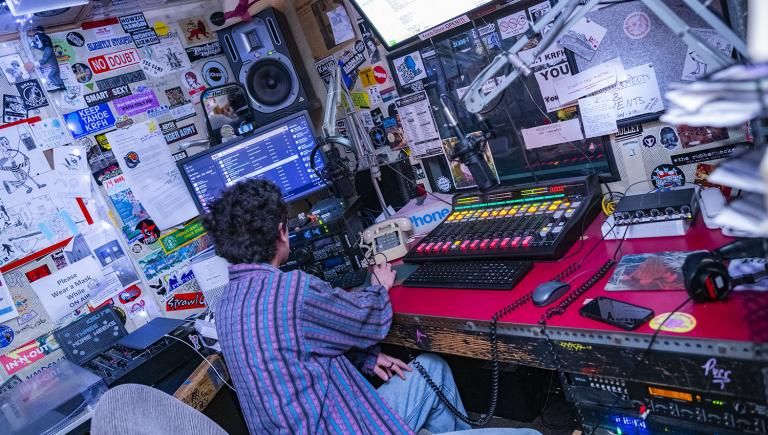 A man in s striped shirt sitting at a radio DJ booth