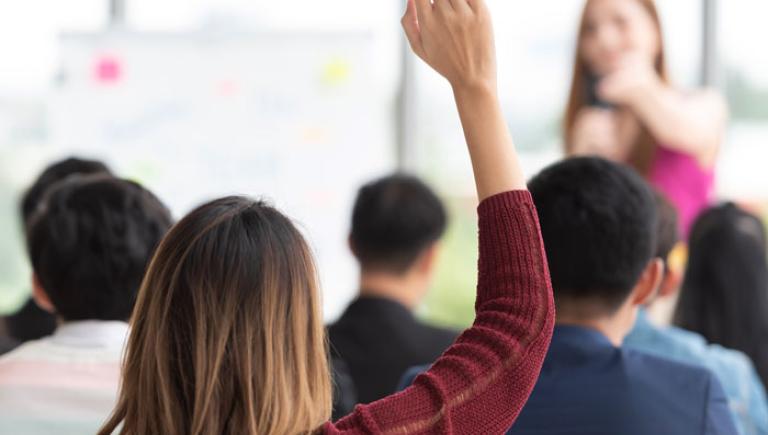 Student raising her hand in college classroom