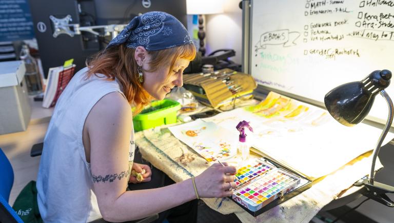 Student employee painting and illustrating for a book in the Press