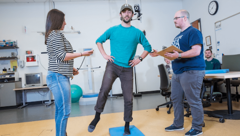 two people talking to one person standing on one foot on a blue mat