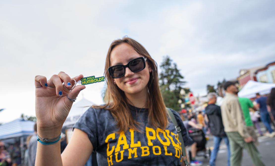 A Cal Poly Humboldt student with a Cal Poly Humboldt shirt holds a small piece of swag at the Arcata Night Market 2025.