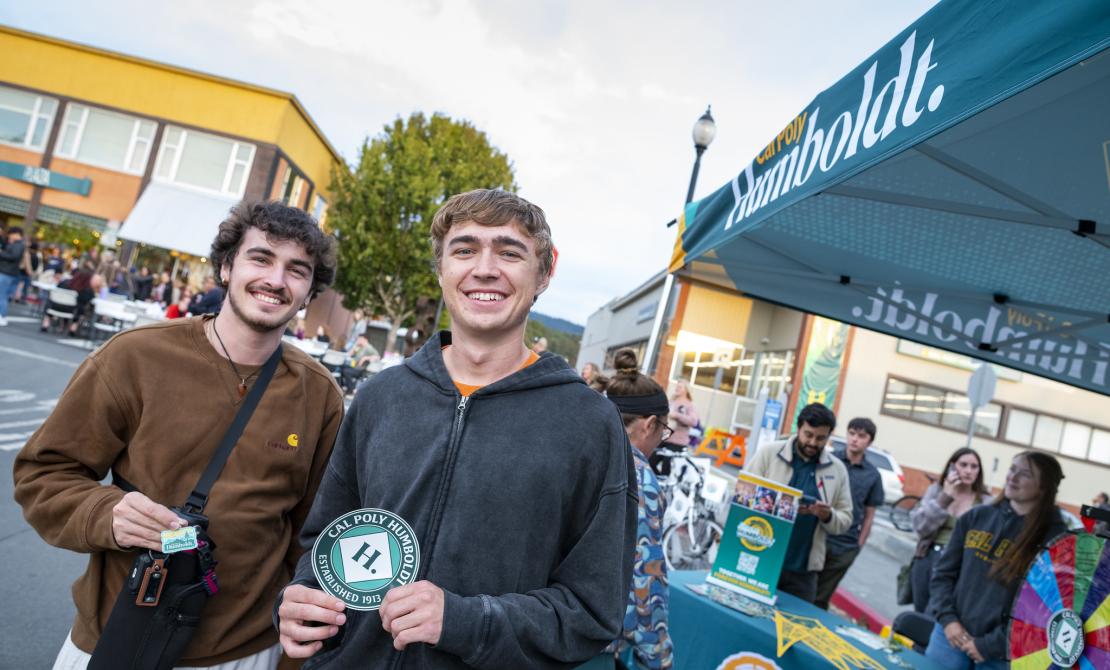 Two Cal Poly Humboldt students with their swag receive from the Forever Humboldt table at Arcata Night Market 2025