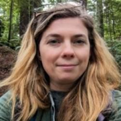 Person wearing a green shirt with a forest in the background.