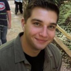 Person wearing green shirt with a walkway, railing, and greenery in the background