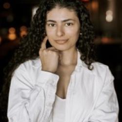 A person wearing a white long-sleeved shirt. Outside at nighttime with colorful lights on buildings in the background.