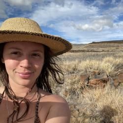 Person wearing a brimmed hat, with grassland in the background