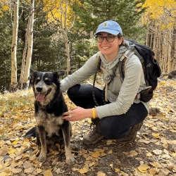Person crouching next to a dog, outside with trees in background