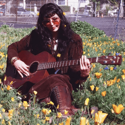Person sitting in a grassy area with flowers, playing a guitar