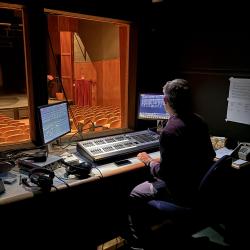 Man in theatre lighting studio with lighting control board in front of him, below two computer screens.