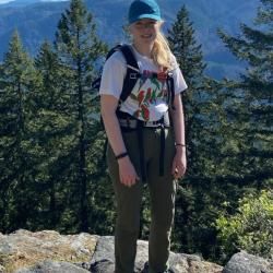 Deirdre standing out in the wilderness with a backpack and blue baseball had